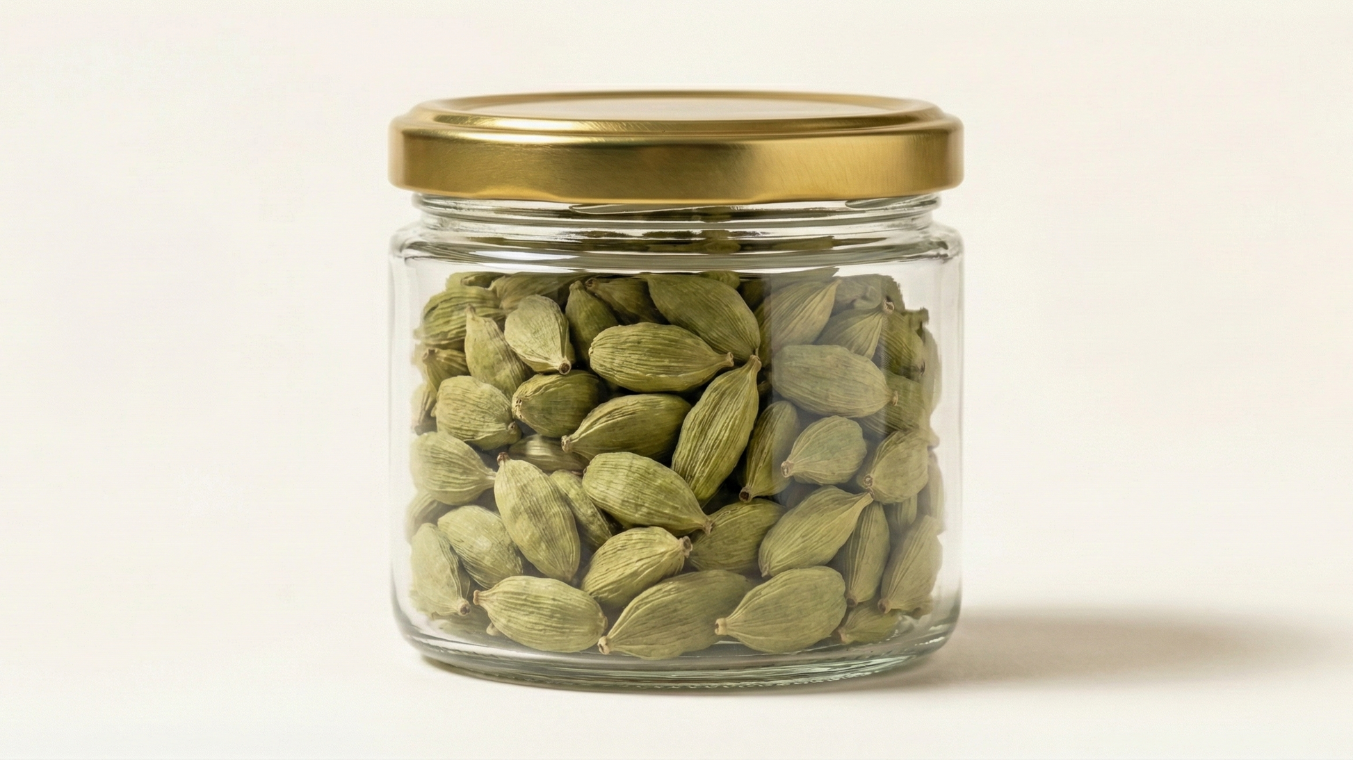 Jar of green cardamom pods with a gold lid on a beige background